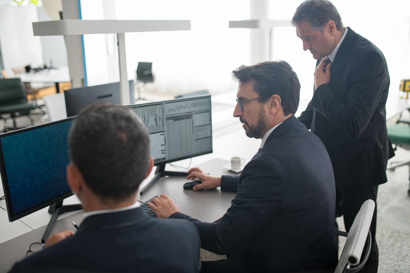Two colleagues reviewing market data across several monitors in an office